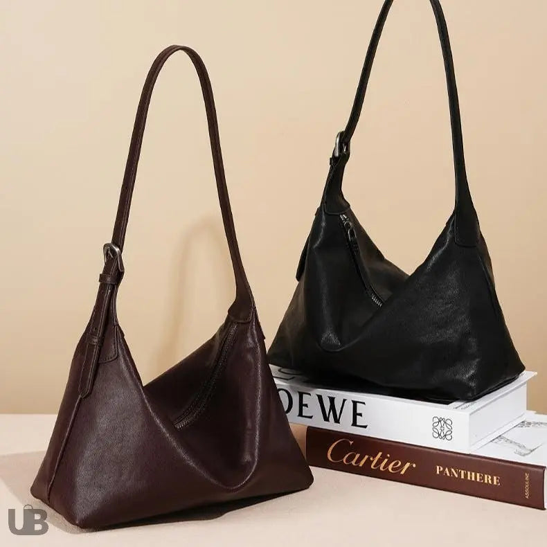 deux sacs fourre tout en cuir véritable l'un marron et l'autre noir , posés sur un support décoratif , et sur deux livre épais
