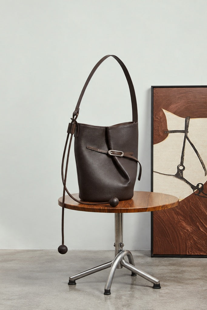 Sac Isabella marron café posé sur une chaise en bois devant un tableau