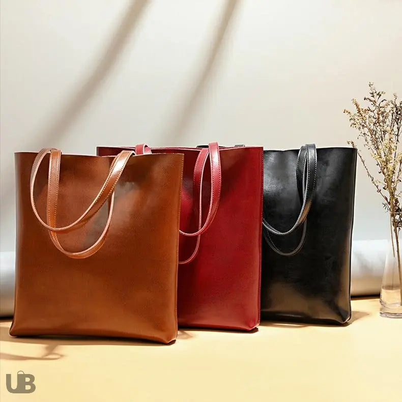 sac_fourre_tout_Luanda-en-cuir-trois modeles camel rouge et noir disposés l'un devant l'autre couvrant la moitié du sac de derrière , sur un meuble avec de la décration