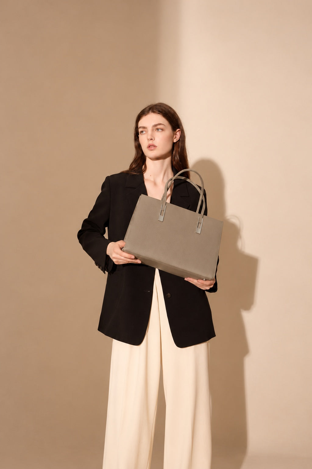 Sac Melinda taupe tenu devant soi par un modèle en blazer noir