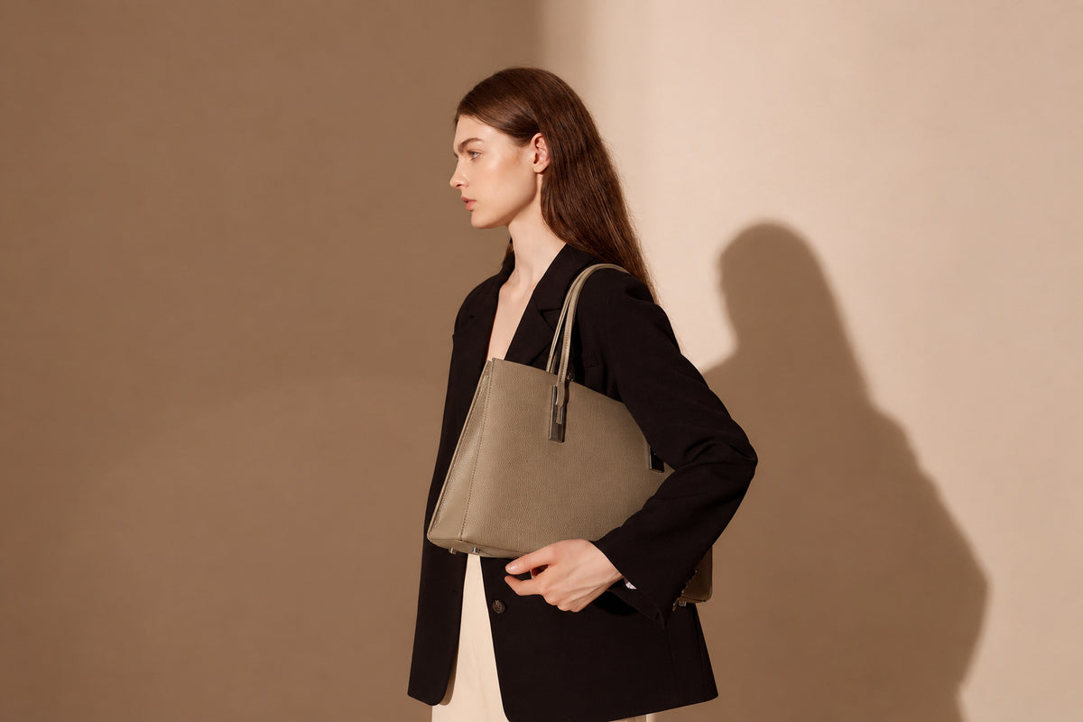 Sac Melinda taupe porté à l’épaule de profil dans un décor beige élargi