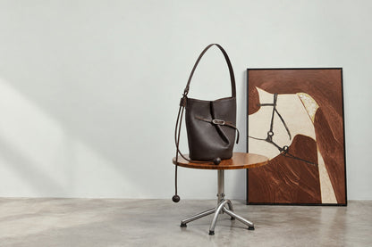 Sac Isabella marron café posé sur une chaise en bois devant un tableau